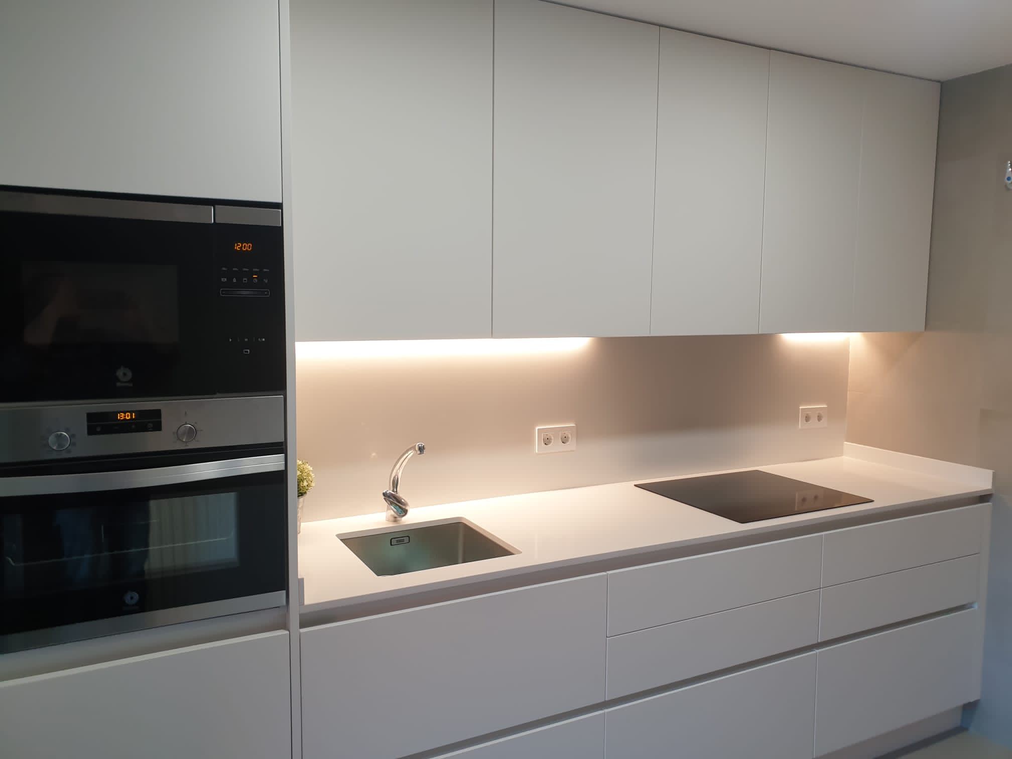 Cocina blanca minimalista con encimera compacta e iluminación cálida