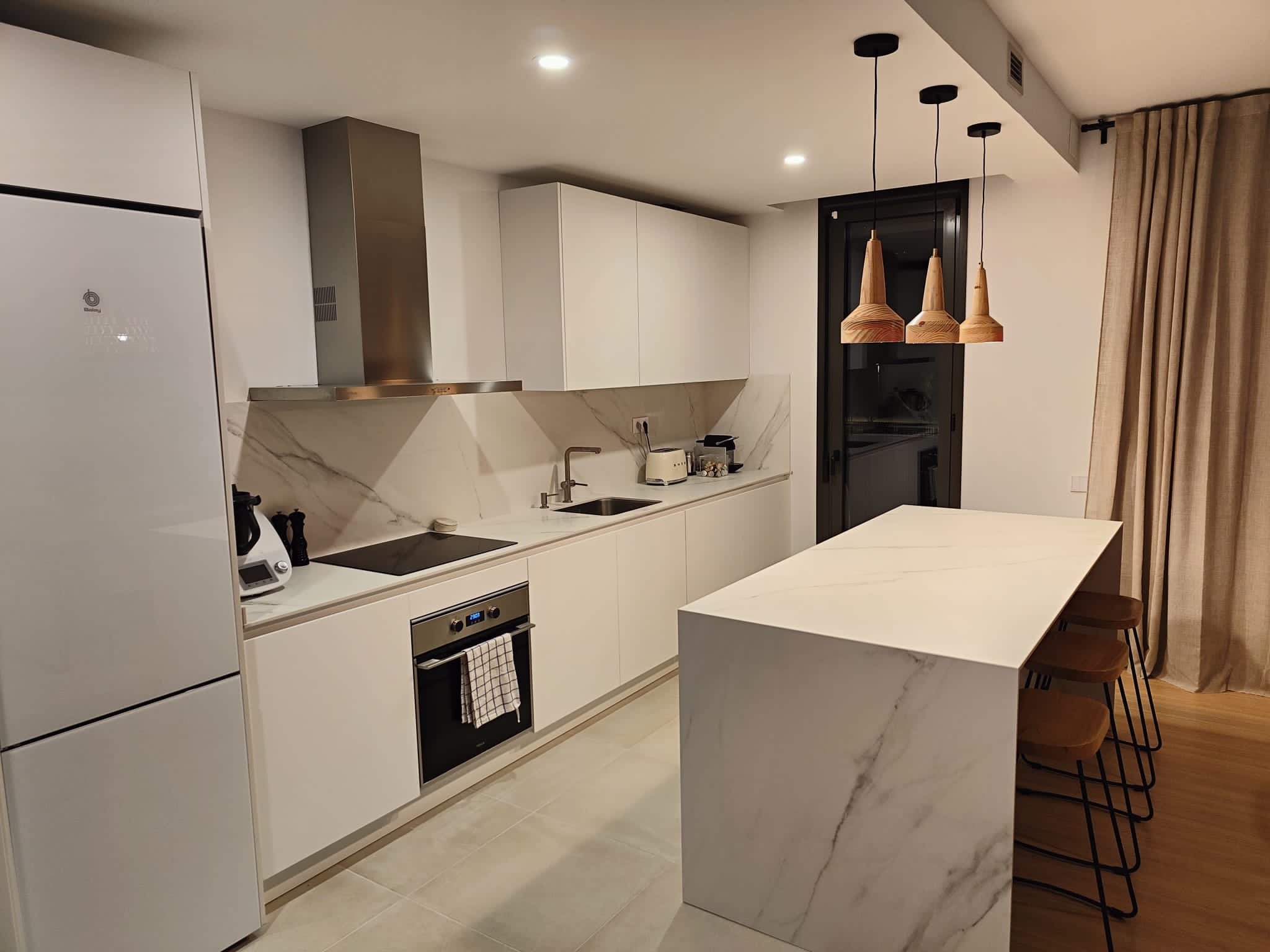 Cocina con isla de mármol y lámparas de madera